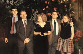 The Savelli family is posing in formal attire in front of a decorated Christmas tree.