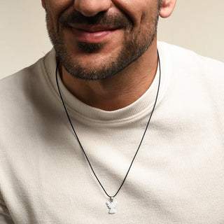 A close-up of a man wearing a Silver angel pendant on a black cord, paired with a cream-colored ribbed t-shirt against a light beige background.
