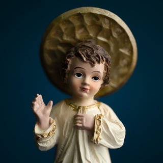 close up of a Child Jesus blessing statue in ivory and gold robe, standing on a blue starred globe, set against a dark blue background.