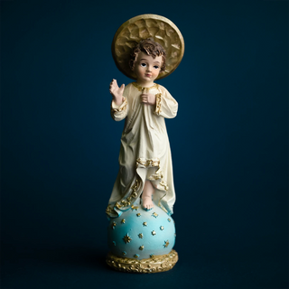a Child Jesus blessing statue in ivory and gold robe, standing on a blue starred globe, set against a dark blue background.