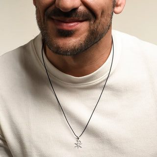 A close-up of a man wearing a Christogram pendant on a black cord neckalce, paired with a cream-colored ribbed t-shirt.