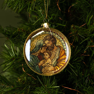 Decorative ornament with a religious scene of the holy family, hanging on a Christmas tree.