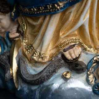 Close-up detail of a Immaculate Conception statue in hand-painted resin, showing draped cream fabric with gold trim, blue fabric at the top, a gray snake wrapping around the base