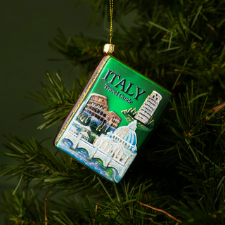 Decorative ornament shaped like a travel guide book with Italian landmarks on a green background, hanging on a tree.