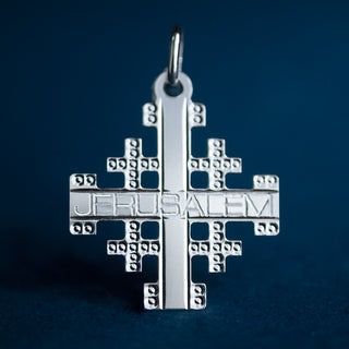 close-up of a Jerusalem cross in sterling silver against a navy blu background