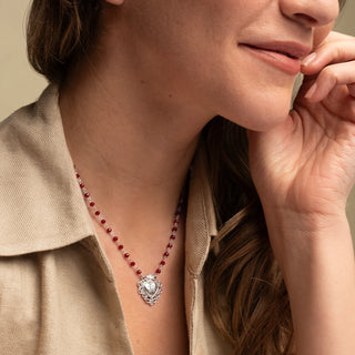 Close-up of a woman wearing a Necklace with red beads and a silver sacred heart-shaped pendant 