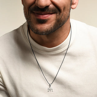 A close-up of a man wearing a silver Virgin Mary Monogram Necklace in Steel with Rubber Cord, paired with a cream-colored ribbed knit shirt.