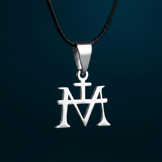 A close-up of a silver Virgin Mary Monogram Necklace in Steel with Rubber Cord against a dark teal background.